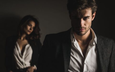 Man displaying narcissistic traits in sharp focus with a drained, dependent woman in the background, illustrating the emotional imbalance and energetic disruption caused by narcissistic relationships.